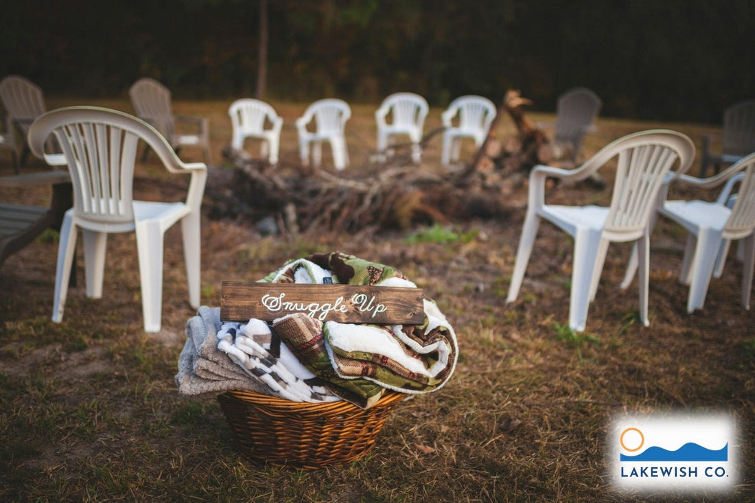 White plastic chairs surround a campfire. IN the front of the image is a wicker packet that has a blanket, plus a sign that says "Snuggle Up."